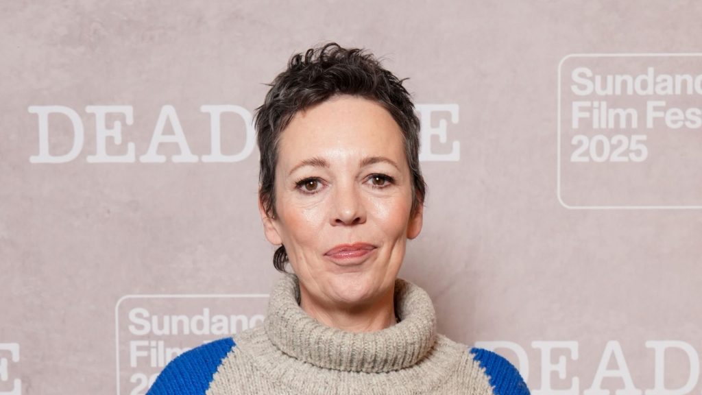 Olivia Colman veste jeans a gamba larga con maglione argyle e sneakers di suede.
