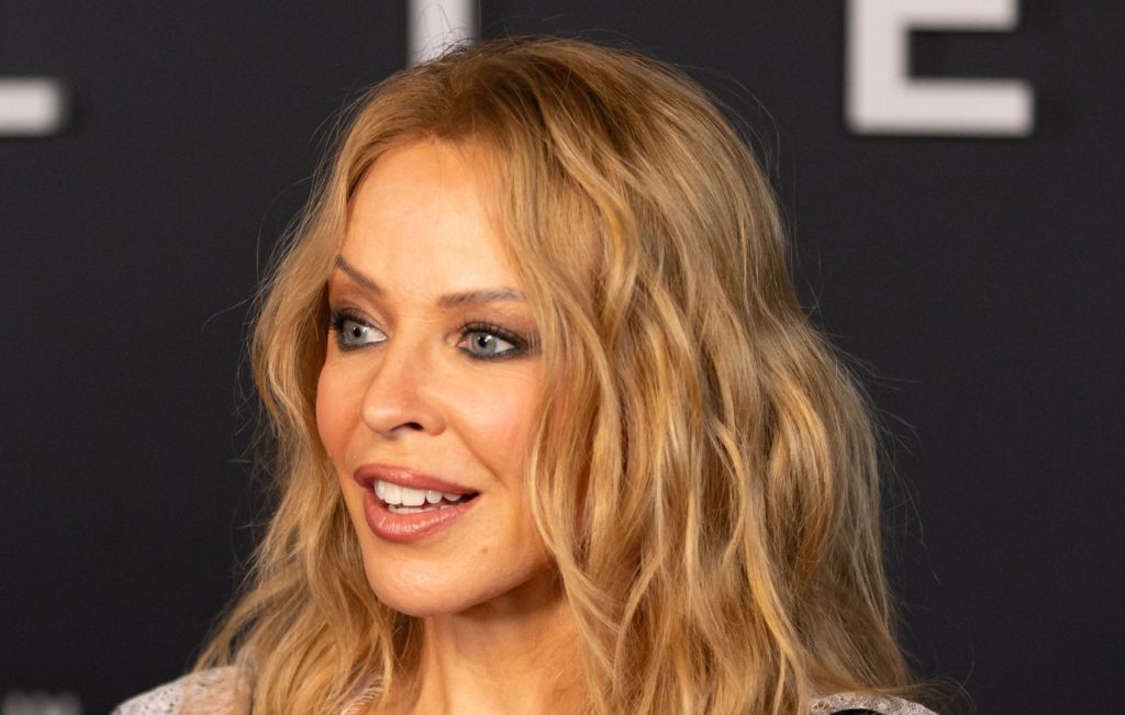 Kylie Minogue brilla in giacca colorata e jeans neri, un look audace e alla moda.