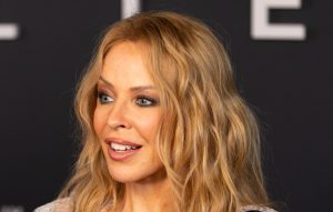 Kylie Minogue brilla in giacca colorata e jeans neri, un look audace e alla moda.