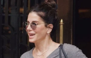 Sandra Bullock’s autumn outfit: grey jumper, relaxed trousers, playful ballet flats.
